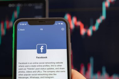 Facebook hisse senedi fiyatları yükseldi ve arka planda grafikler var. Ekranda logosu olan akıllı telefonu tutan adam elleri, Şubat 2022, San Francisco, ABD