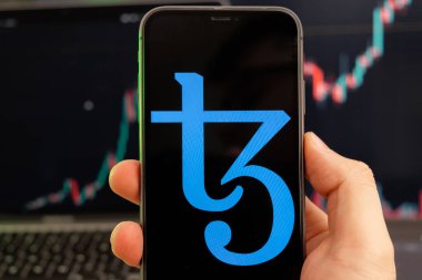 Tezos XTZ şifreleme logosu erkek eliyle akıllı telefon ekranında yeşil arka planda giderek artan bir eğilimle 