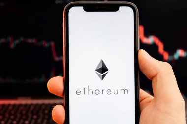 İnsan eliyle cep telefonu ekranındaki kripto döviz piyasası analizinin Ethereum ETH uygulaması ve arka plandaki eğilim grafikleri, Şubat 2022, San Francisco, ABD