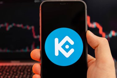 KuCoin Token KCS şifreleme borsa analizi uygulaması insan eliyle cep telefonu ekranında ve logaritma grafiklerinde arka planda ticaret verileri, Şubat 2022, San Francisco, ABD