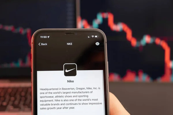Nike tendência de baixa do preço das ações com gráficos vermelhos em segundo plano. Mãos de homem segurando um smartphone com logotipo na tela, fevereiro de 2022, San Francisco, EUA — Fotografia de Stock
