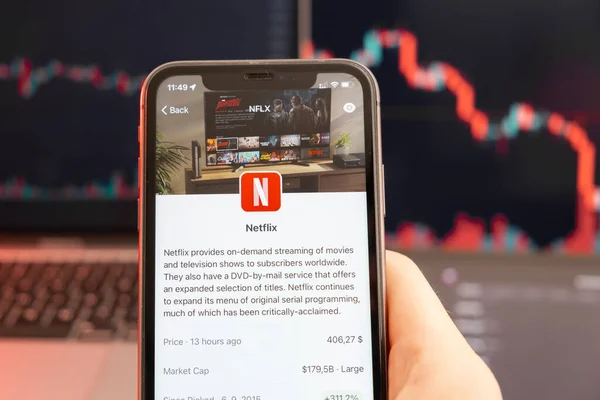 Netflix tendência de baixa do preço das ações com gráficos vermelhos em segundo plano. Mãos de homem segurando um smartphone com logotipo na tela, fevereiro de 2022, San Francisco, EUA — Fotografia de Stock
