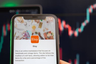 Arka planda grafiklerle Etsy hisse senedi fiyatları yükseldi. Ekranda logosu olan akıllı telefonu tutan adam elleri, Şubat 2022, San Francisco, ABD