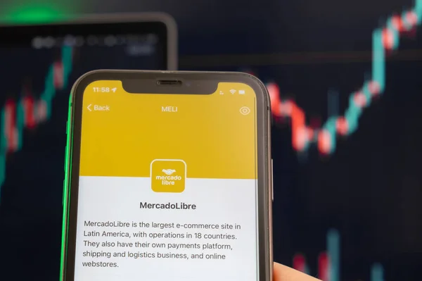 MercadoLibre Aktienkurs Aufwärtstrend mit Graphen auf dem Hintergrund. Männliche Hände halten ein Smartphone mit Logo auf dem Bildschirm, Februar 2022, San Francisco, USA — Stockfoto