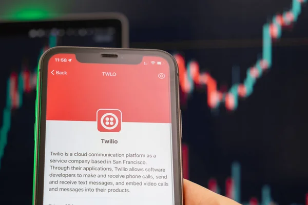 Twilio preço das ações tendência de alta com gráficos em segundo plano. Mãos de homem segurando um smartphone com logotipo na tela, fevereiro de 2022, San Francisco, EUA — Fotografia de Stock