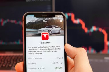 Tesla Motors hisse senedi fiyatları düşüşte ve arka planda kırmızı grafikler var. Ekranda logosu olan akıllı telefonu tutan adam elleri, Şubat 2022, San Francisco, ABD