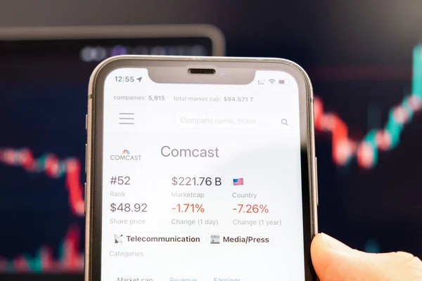 Preço das ações da Comcast na tela do celular em mão de homem com gráficos de mercado de ações em mudança em segundo plano, fevereiro de 2022, San Francisco, EUA — Fotografia de Stock
