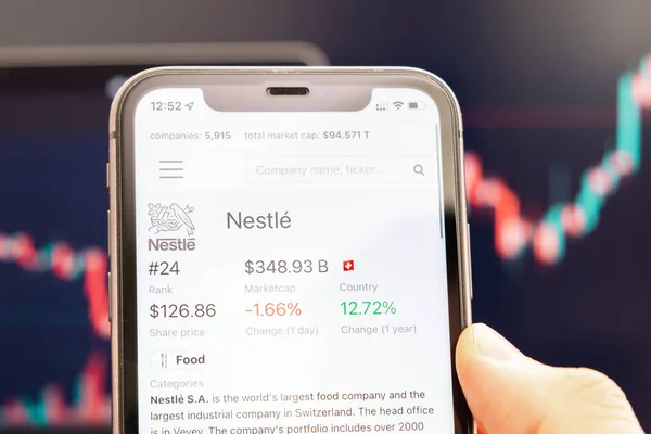 Nestlé-Aktienkurs auf dem Bildschirm des Mobiltelefons in der Hand mit sich verändernden Börsenkursen im Hintergrund, Februar 2022, San Francisco, USA — Stockfoto