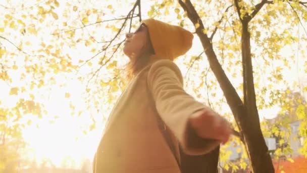 Filmagem cinematográfica de uma mulher feliz em roupas casuais, casaco marrom e chapéu laranja girando em uma floresta de outono ensolarada — Vídeo de Stock
