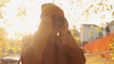 Kamera, genç bir kadın fotoğrafçının sonbahar parkında gün batımında fotoğrafını çekiyor.
