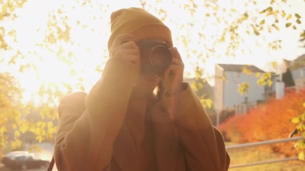 La cámara gira alrededor de una joven fotógrafa tomando una foto al atardecer en un parque de otoño — Vídeo de stock
