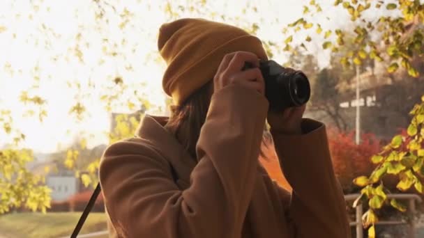 La cámara gira alrededor de una joven fotógrafa tomando una foto al atardecer en un parque de otoño — Vídeos de Stock