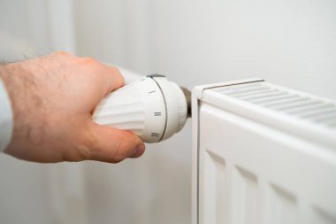 İnsan eli ısıtma maliyetlerini düşürmek için ısıtma radyatörünün ısı düğmesini düzenler..