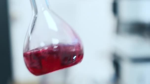 Лабораторная колба с жидкостью, встряхнутой на размытом фоне — стоковое видео