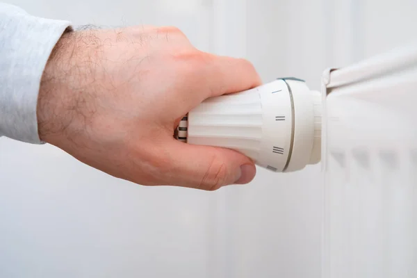 La mano del hombre regula la perilla de temperatura del radiador de calefacción para reducir los costos de calefacción. — Foto de Stock