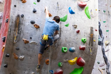 Tırmanışçı yapay kaya duvarında, kayalık jimnastik salonunda sigorta yaptırıyor.
