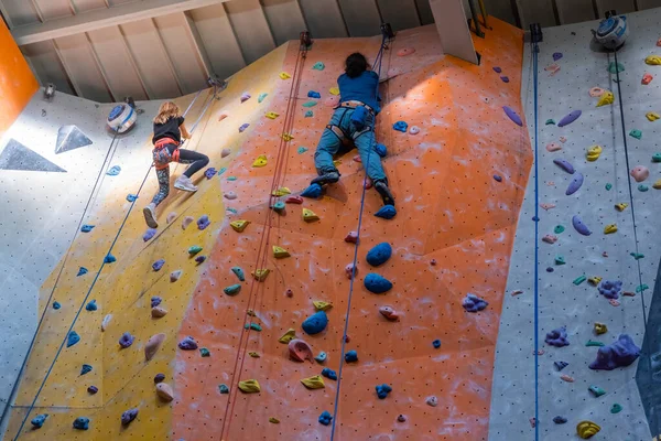 Klättrarna tränar på konstgjord bergvägg med försäkring i bouldering gym — Stockfoto