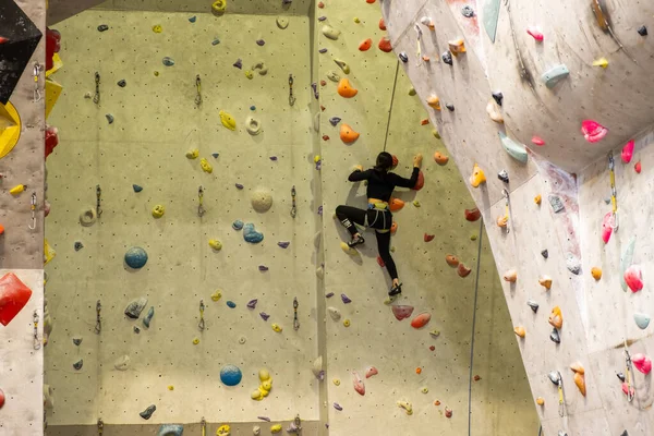 Der Kletterer trainiert an der künstlichen Felswand mit Versicherung in der Boulderhalle — Stockfoto