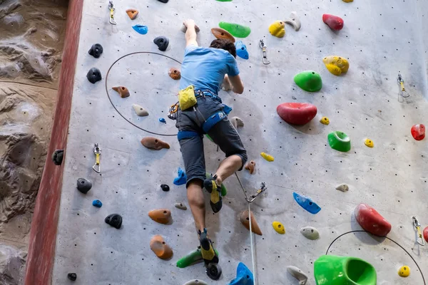 O alpinista treina na parede de rocha artificial com seguro no ginásio de pedregulho — Fotografia de Stock