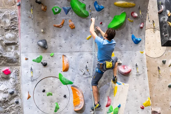 Klättraren tränar på konstgjord bergvägg med försäkring i bouldering gym — Stockfoto