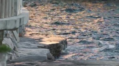Deniz dalgaları, gün batımında yosun ile beton döker.