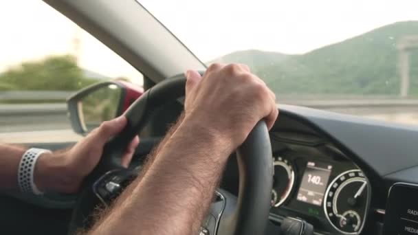 Mann hält Lenkrad von Auto, das an Bergen vorbeifährt — Stockvideo