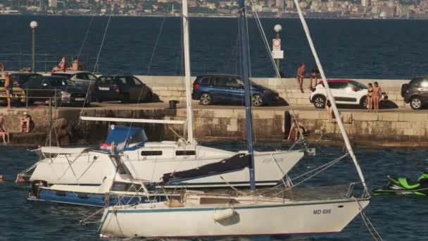 Jetée de mer avec des voitures garées yachts amarrés et les gens de natation — Video