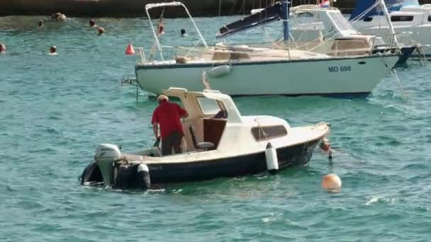 De mens bereidt zich voor om te zeilen op een motorboot afgemeerd in de buurt van jachten — Stockvideo