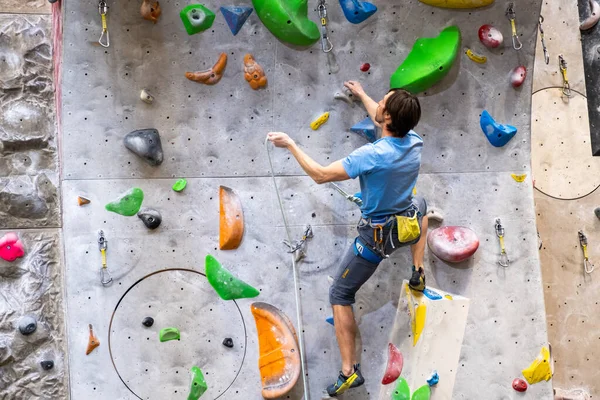 Tırmanışçı yapay kaya duvarında, kayalık jimnastik salonunda sigorta yaptırıyor.