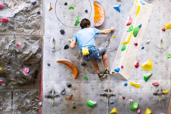 Klättraren tränar på konstgjord bergvägg med försäkring i bouldering gym — Stockfoto