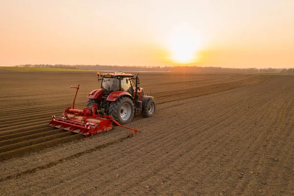 Modern tractor cultivates soil in field at bright sunset — Stock Photo, Image