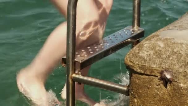 Młoda kobieta wychodzi z morza używając drabiny po kąpieli — Wideo stockowe