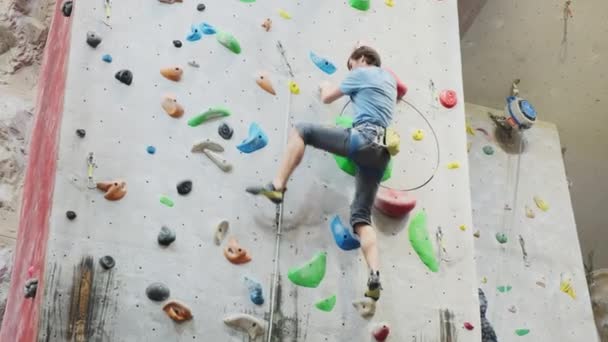 Der Kletterer trainiert an der künstlichen Felswand mit Versicherung in der Boulderhalle — Stockvideo