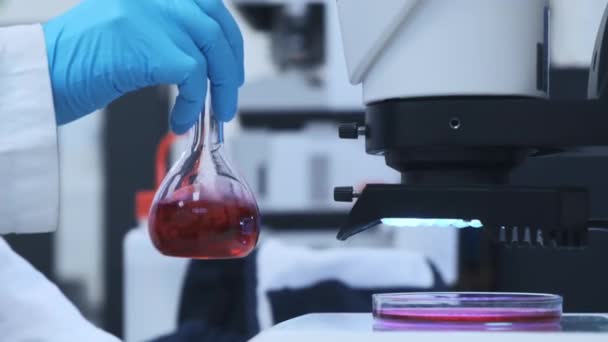 Científico mezclando líquido rosa en los frascos de vidrio — Vídeos de Stock