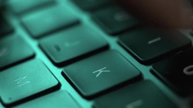 Yakından bir adam dizüstü bilgisayarıyla çalışıyor ve mavi ışıkta siyah klavyeyle yazı yazıyor.. 
