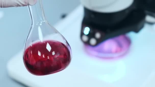 Scientist mixing pink liquid in the glass flasks — Vídeo de Stock