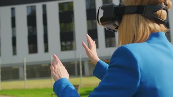 Eine glückliche Frau im Anzug steht draußen und gestikuliert in Augmented Reality mit 3D-VR-Brille — Stockvideo