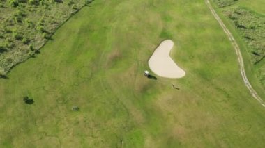 Kırsal bölgedeki yeşil sahada golf arabasının yanında golf oynuyor. Güneşli yaz günlerinde spor ve eğlence için yeşil çimenleri olan geniş bir alan.