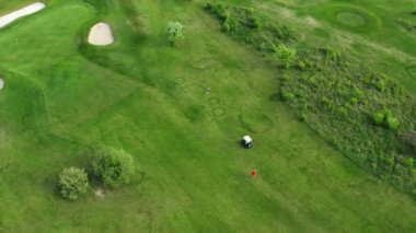 Oyuncular kırsaldaki büyük yeşil golf sahasında duran el arabasının yanında yürürler. Yaz günü havadan izlemek için büyük kırsal alan