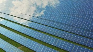 Güneş modülleri elektrik istasyonundaki beyaz bulutları yansıtıyor. Alanda inşa edilen modern fotovoltaik güneş panelleri yeşil enerji hava görüntüsü üretiyor
