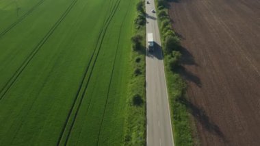 Beyaz kamyon tarlaları geçerek yol alıyor. Kamyon çok önemli malları hızlı taşıyor. Ağaçlar gün batımında tarlaya gölge düşürür.