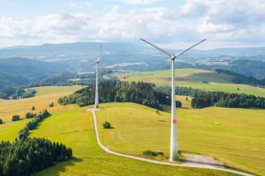 Sarı tarladaki rüzgar türbinlerinin panoramik manzarası ve arka plandaki dağların. Yeşil ve yenilenebilir enerji üretimi. 