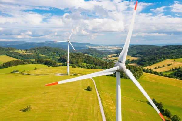 Aerial view of wind turbines propeller in the yellow field with amazing view on the mountains in sunny day. Environment friendly and renewable energy resource.