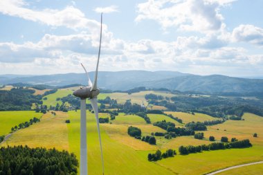 Aerial view of wind turbines propeller in the yellow field with amazing view on the mountains in sunny day. Environment friendly and renewable energy resource. 
