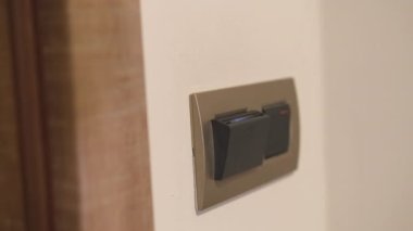 Female person hand puts back key card into room card holder. Woman putting key card switches on light in hotel room on blurry background closeup