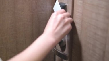 Woman hand puts key card to panel opening hotel room door. Female person with blue nails opening door walks in room on blurry background closeup