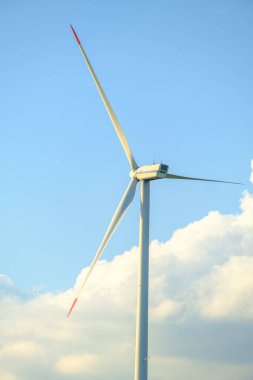 Windmill converts kinetic energy into electrical green energy against blue sky with white clouds. Long blades rotate producing energy closeup
