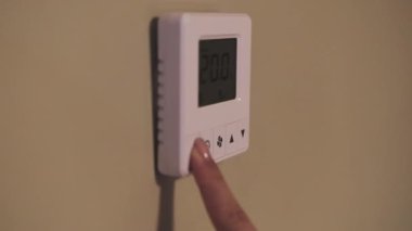 Female person finger switches on temperature controller of air conditioner. Adult woman chooses comfortable temperature of device closeup