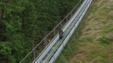 DOLNI MORAVA, CZECH REPUBLIC - MAY 14 2022: Motion along bobsleigh track past green forest landscape. Special sleigh goes up on bobsleigh track along hill slope aerial view on May 14 in Dolni Morava