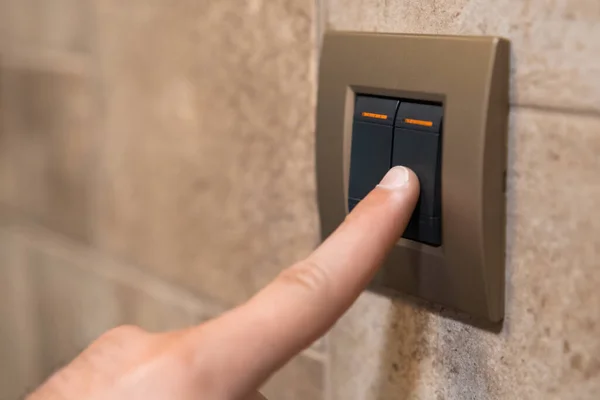 Female person hand switches off light. Adult woman presses light button to turn off light in beige room closeup